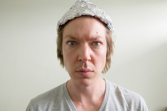 Face of young man wearing tin foil hat inside the room