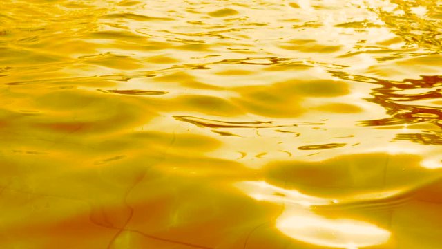 Ripple of water golden water waves surface texture background with light reflections, slow motion