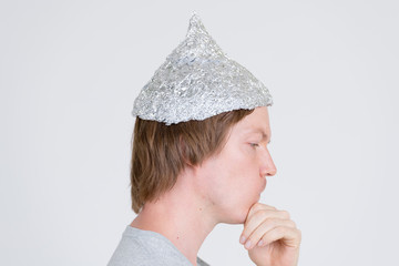 Closeup profile view of young man with tinfoil hat thinking as conspiracy theory concept
