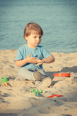 Happy boy sitting on beach and playing with sand. Vacation time concept