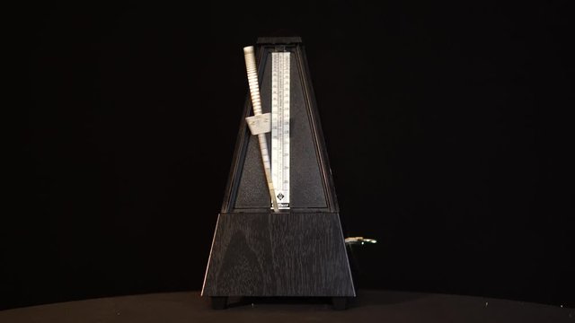 Front view of metronome with pendulum in motion on black-screen, music playing by rhythm