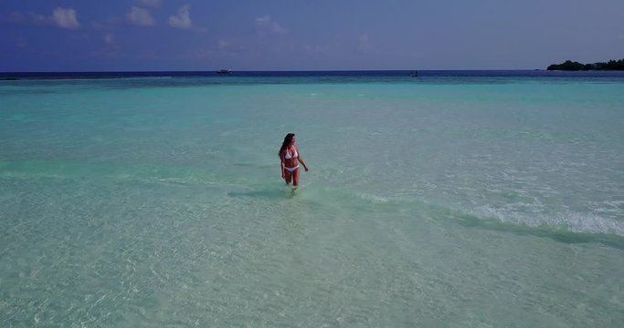 Beautiful young girl in white bikini walking in crystal shallow water off the coast of tiny luscious island in Maldives