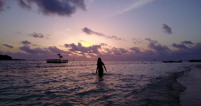 Sunset over water in Malaysia, girl splashing water with pink cloudy sky in the background