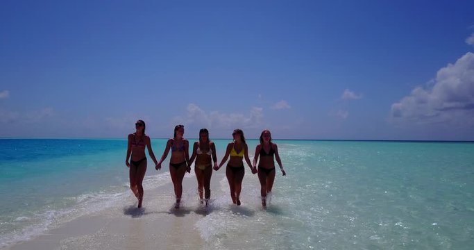 Pretty girls walking holding hands on tiny strip of sand in the middle of the ocean at Bali