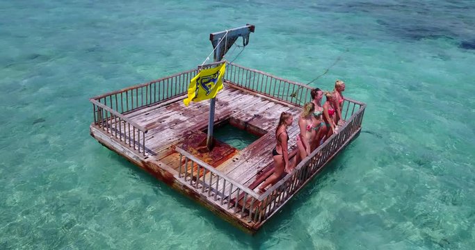 Five young women in bikinis stand and relax on a rusty floating dock in Malaysia