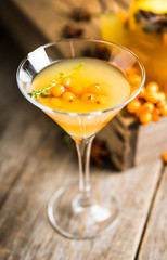 Hot autumn cocktail with sea buckthorn and orange juice in martini glass on the rustic background. Selective focus. Shallow depth of field.