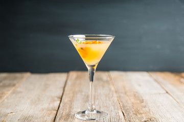 Hot autumn cocktail with sea buckthorn and orange juice in martini glass on the rustic background....