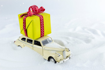 Retro car with gift box on snowy road. Christmas holiday background with toy car with copy space.