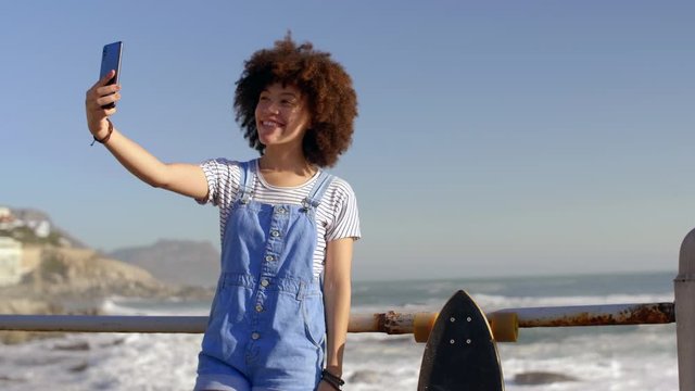 Millennial woman smiling for selfie taking photo with her phone cellphone mobile by the ocean