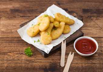 Buttered chicken nuggets on chopping board with wooden forks and ketchup on wooden background.