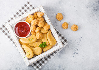 Buttered chicken nuggets and popcorn bites in white vintage wooden box with ketchup on light background. Top view