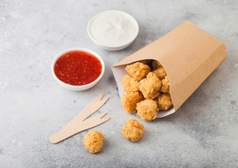 Crunchy southern chicken popcorn bites in paper container for fast food meals on light background. Sweet chilli and sour cream sauce