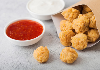 Crunchy southern chicken popcorn bites in paper container for fast food meals on light background. Sweet chilli and sour cream sauce