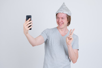 Happy young man with tin foil hat taking selfie and showing peace sign