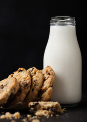 Homemade organic oatmeal cookies with raisins and apricots and bottle of milk on dark wooden background.