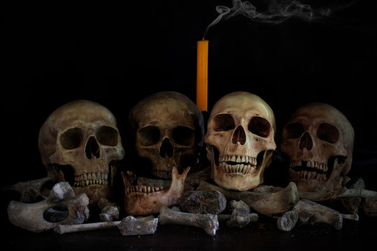Skulls and pile of bones on dark background with candle which has smoke
