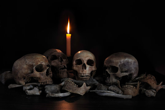 Skulls and pile of bones on dark background with light candle
