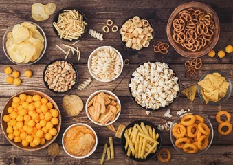 Foto op Aluminium All classic potato snacks with peanuts, popcorn and onion rings and salted pretzels in bowl plates on wooden background. Twirls with sticks and potato chips and crisps with nachos and cheese balls. © DenisMArt