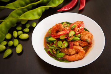 Stir-Fried Twisted Cluster Bean with Shrimps in white dish on wooden table. The Southern Thai food made from Bitter Bean and shrimps.