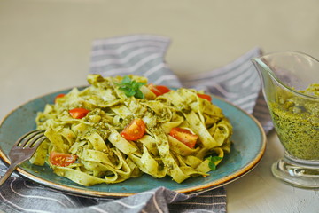 Italian food - fettuccine pasta with pesto sauce, cherry tomatoes, pine nuts and parmesan cheese on concrete background. Selective focus.