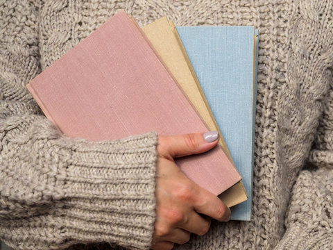 A stack of books in women's hands. Girl in a wool sweater holds in his hand a colorful book. Cozy atmosphere