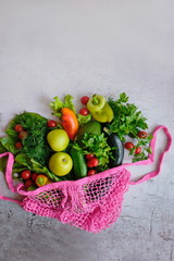 Fresh green and red vegetables and fruits in pink meshon on grey background. Top view. Healthy food, natural products. Concept-reusable bag. Copy space.