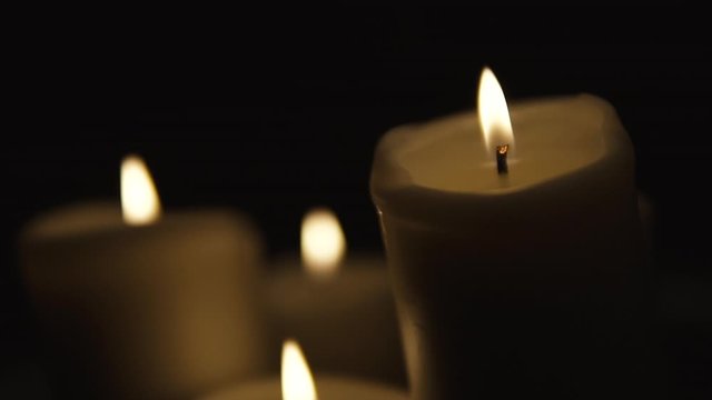 Sharp image of a candle in the foreground, Static shot of group lighted candle,  composition on black background, slow motion