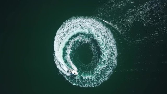 Aerial bird view of a speedboat riding in a circle and making beautiful round path in the sea. speed boat making donuts in 4K in the middle of the ocean