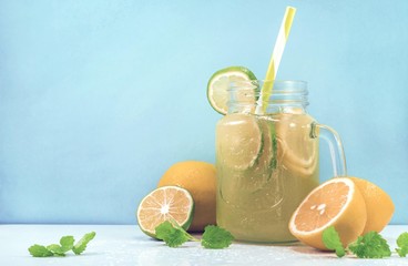 Lemonade drink of soda water, citrus and mint on the light blue background. Cocktail glass with...
