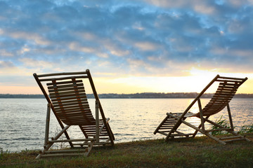 Empty wooden deckchairs on hill near calm river