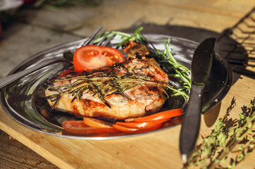 Steak cooking on grill served on a plate with spices, herbs and tomatoes. Food background with barbecue party, front view