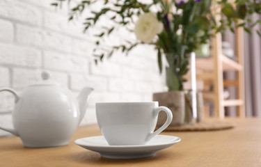 Fototapeta na wymiar Teapot, cup and flowers on wooden dining table indoors. Kitchen interior