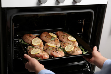 Woman putting chicken breasts with lemon and rosemary into oven, closeup