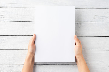 Female hands holding empty paper sheet on white wooden background. Top view