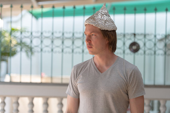 Young man with tin foil hat thinking as conspiracy theory concept outdoors