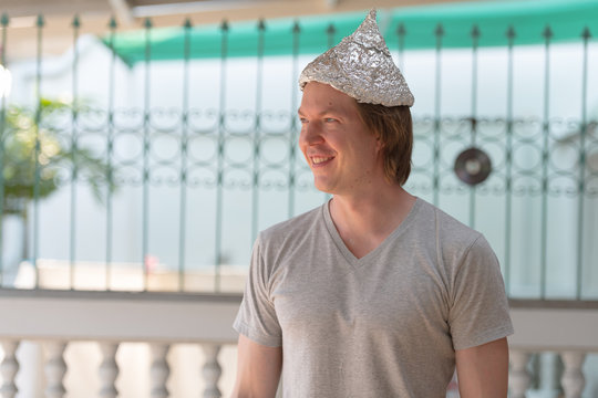 Happy young man with tin foil hat thinking as conspiracy theory concept outdoors