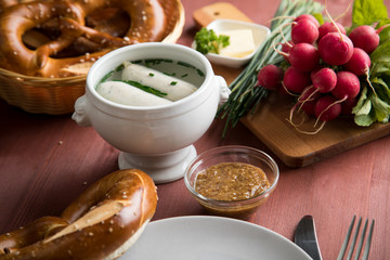 Münchener Weißwurst in Terrine mit bayrischer süßen Senf, Brezel, Radieschen, Schnittlauch und Butter auf Holz Tisch