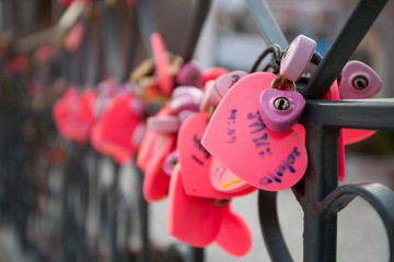 Fototapeta na wymiar Close-up on locks of hearts in different colors and shapes hanging on the fence as a sign of eternal love, which is hung during the wedding.