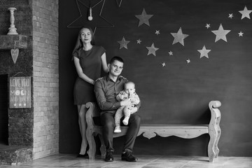 Fototapeta na wymiar Parents and their child sitting on a bench. Mom, dad and baby. Portrait of young family. Happy family life. Man was born. On gray wall gold stars.