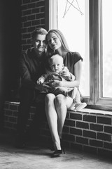 Naklejka premium Parents and their child sitting at the window. Mom, dad and baby. Portrait of young family. Happy family life. Man was born.