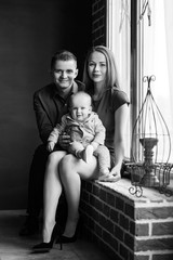 Parents and their child sitting at the window. Mom, dad and baby. Portrait of young family. Happy family life. Man was born.