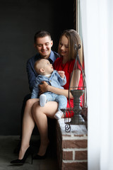 Obraz premium Parents and their child sitting at the window. Mom, dad and baby. Portrait of young family. Happy family life. Man was born.