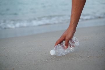 Close up of hand picking up plastic bottle (PET) trash on the beach with sea and sand background....