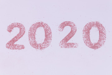 2020 number made of small particles of pink sand on white background