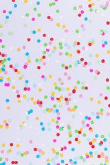 A pattern of multicolored shiny confetti scattered randomly on white background