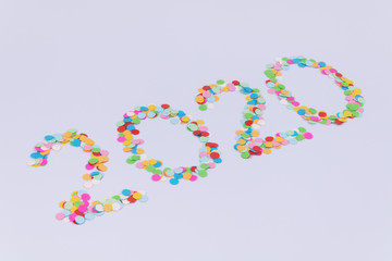 Side view of an inscription of number 2020 new year made of multicolored confetti on a white background