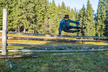 Young male farmer in a denim jacket and cowboy hat jump over the fence