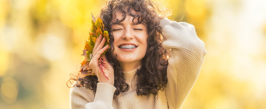 Young woman full of emotions from autumn season. Girl with a dental braces and curly hair