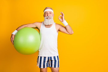 Photo of aged model white hair guy hold green fit ball showing okey symbol advice great trainer wear tank-top striped shorts sweatband isolated yellow color background - obrazy, fototapety, plakaty