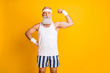 Photo of cheerful positive attractive handsome old man demonstrating his muscles looking intently at you holding hand on waist isolated vivid color yellow background - obrazy, fototapety, plakaty